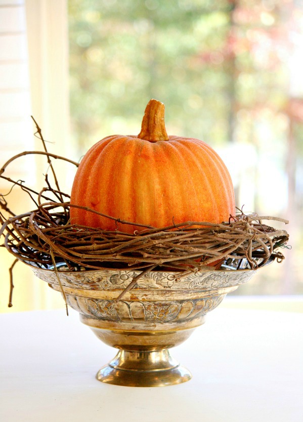 The start of a fall floral arrangement using a grapevine wreath and faux pumpkin.