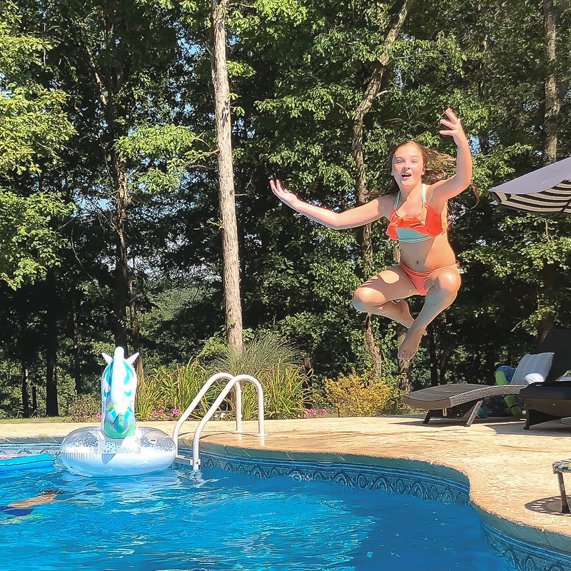 girl jumping in a pool with unicorn float