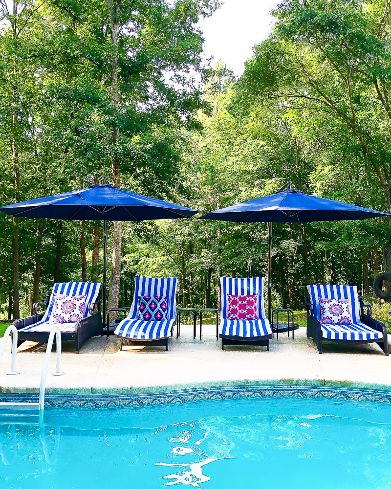 four chaise lounge chairs with stripe towels and pillows poolside