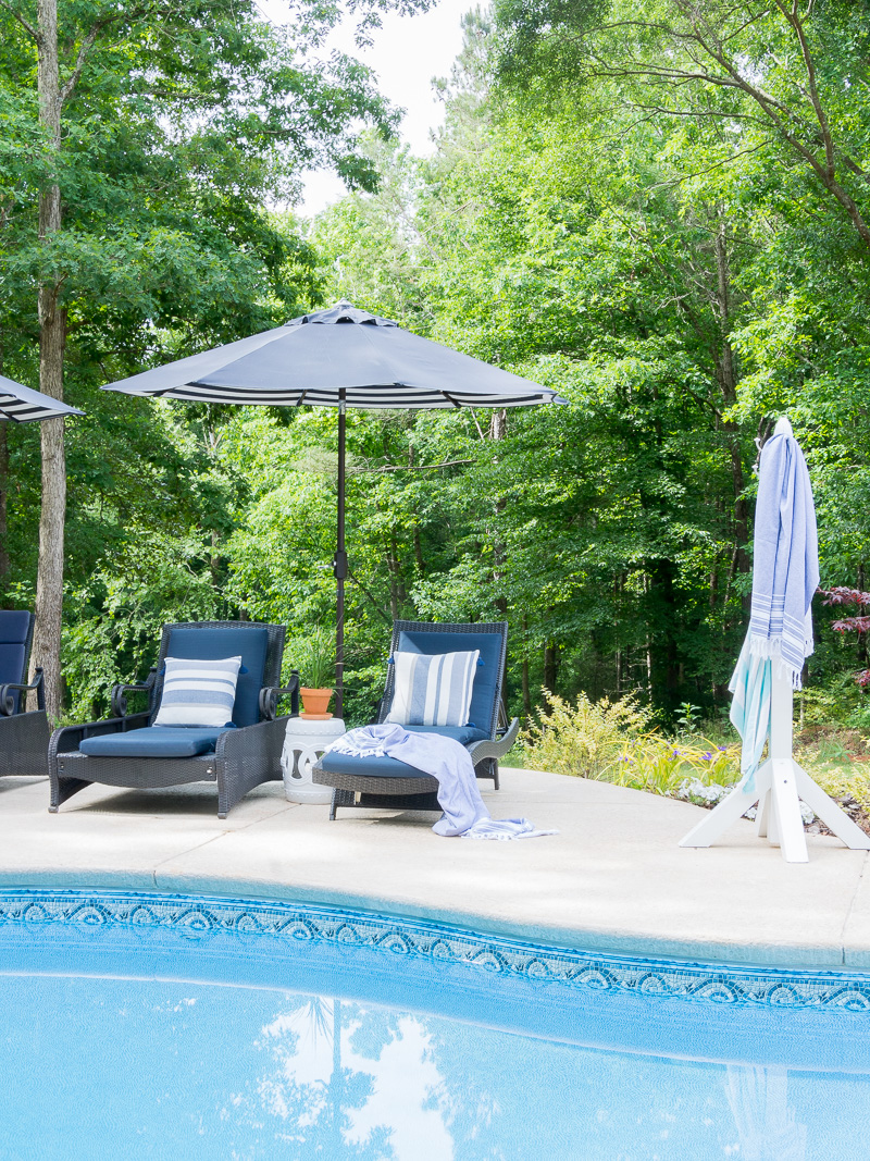 umbrella, lounge chairs and towel rack on a pool deck.