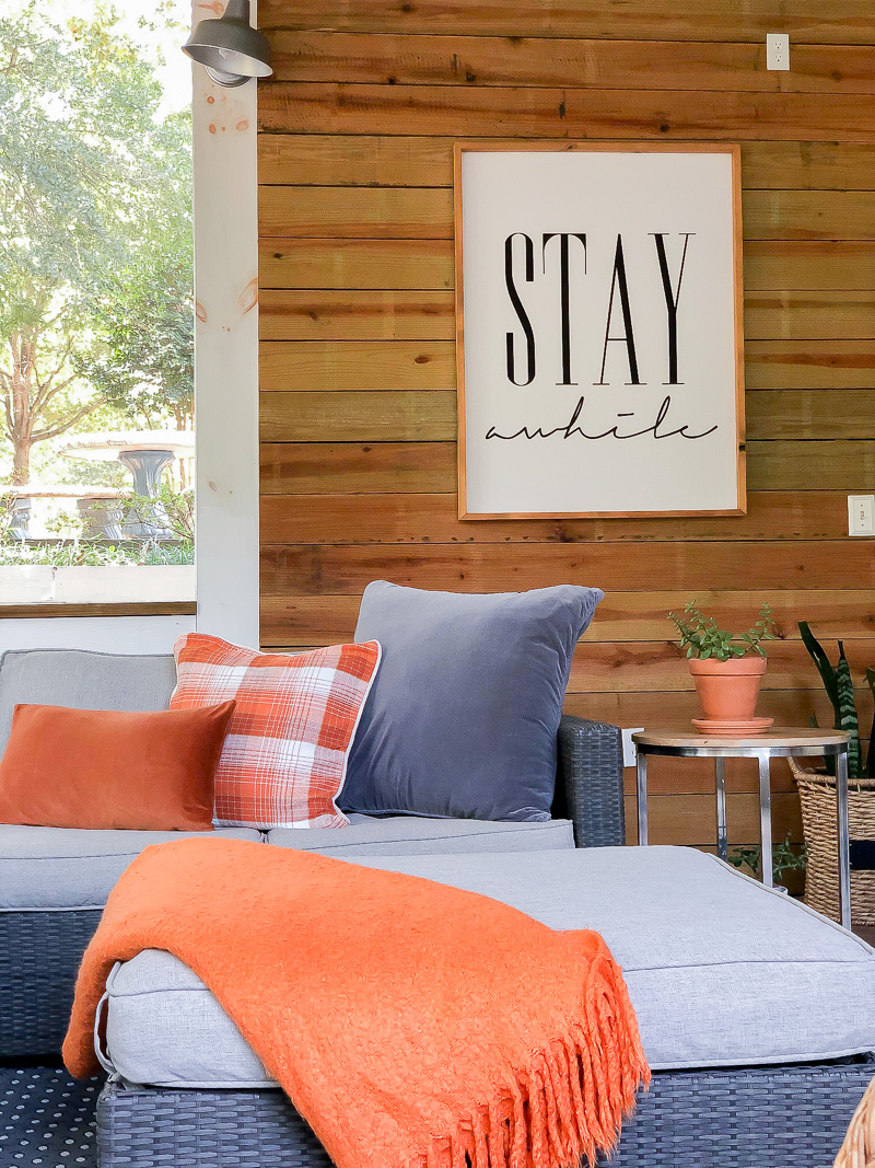 Sectional with gray and orange pillows with ottoman with a orange blanket draped over the corner.