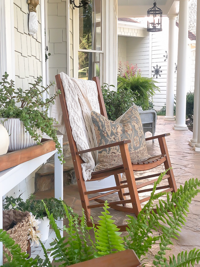 Outdoor front porch with wood rockers with cream throw blanket draped on the back with pillow on it.