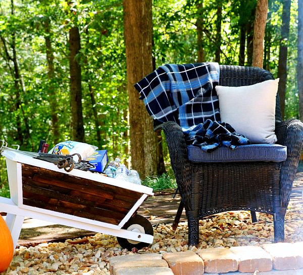 Black chair with blanket with a wheelbarrow with supplies for campfire and smores.