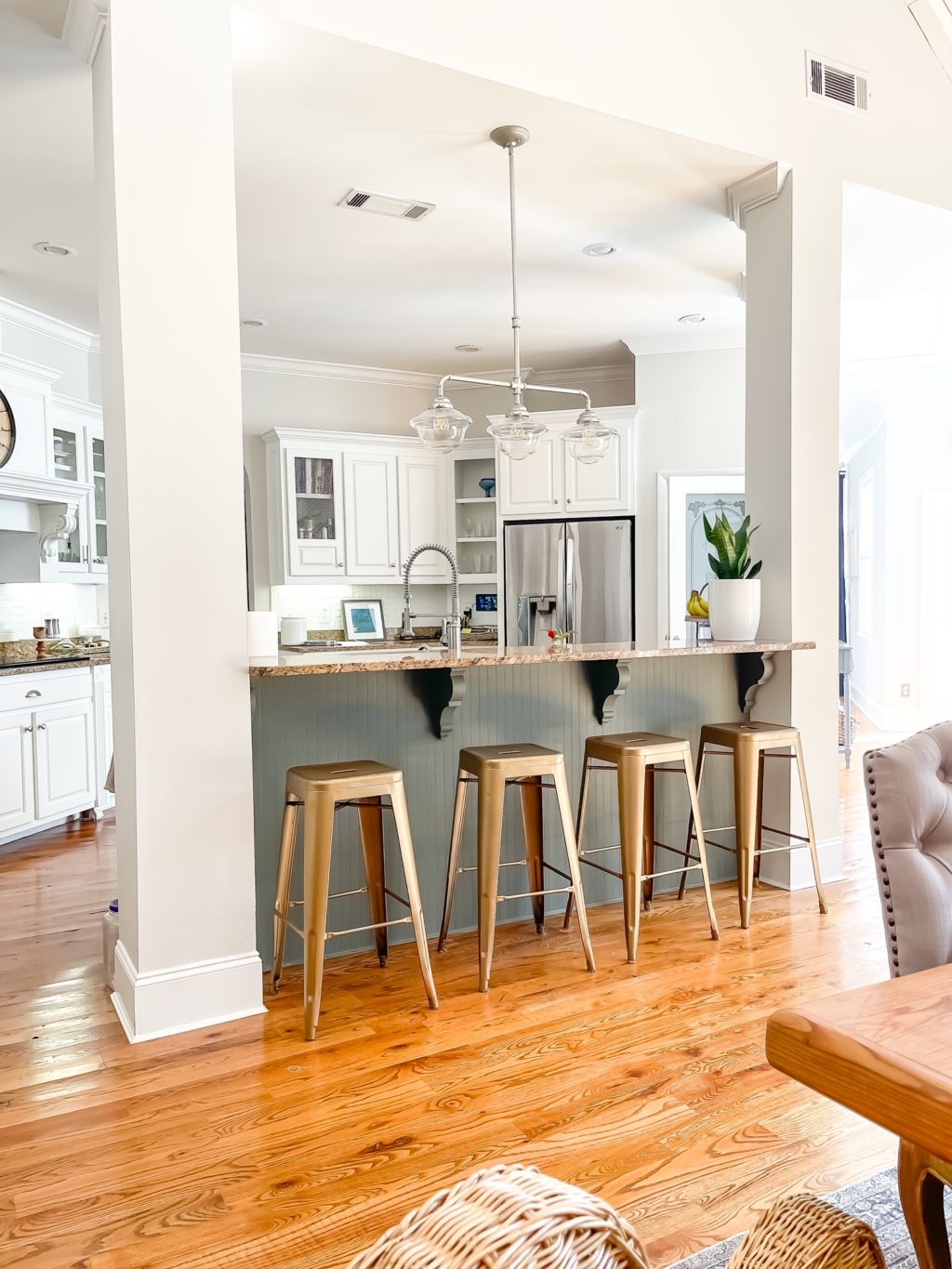 View into a kitchen with white cabinets and green island with brass colored bar stools.