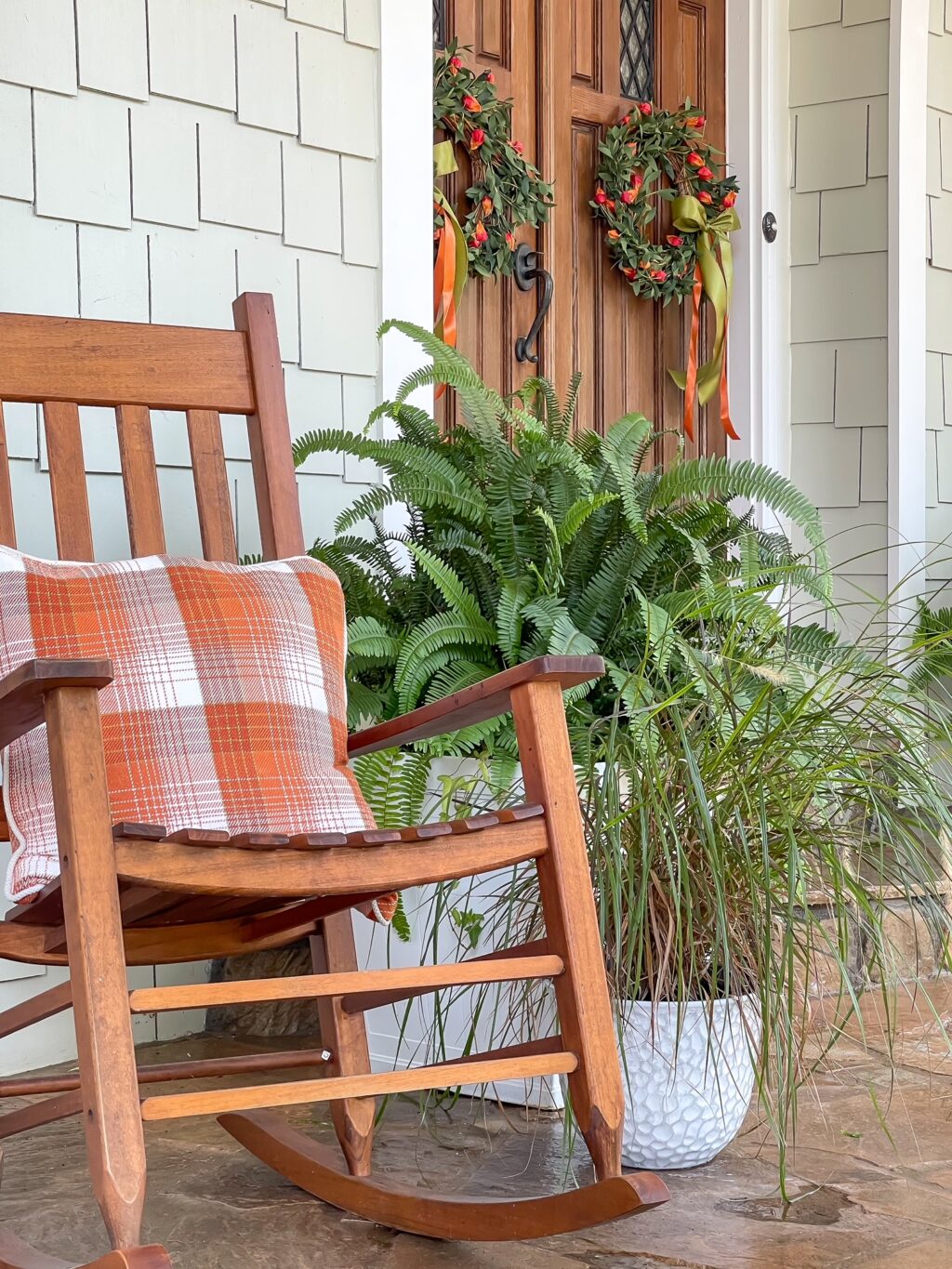 Wood rocker with a plaid orange pillow with wreaths on the front doors.