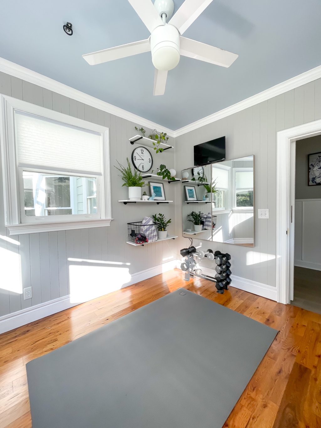 Home gym with gray walls and white trim with mirrored wall with shelves.