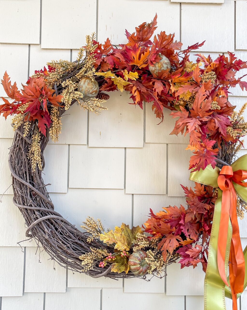 grapevine wreath with fall floral stems and green and orange ribbon.