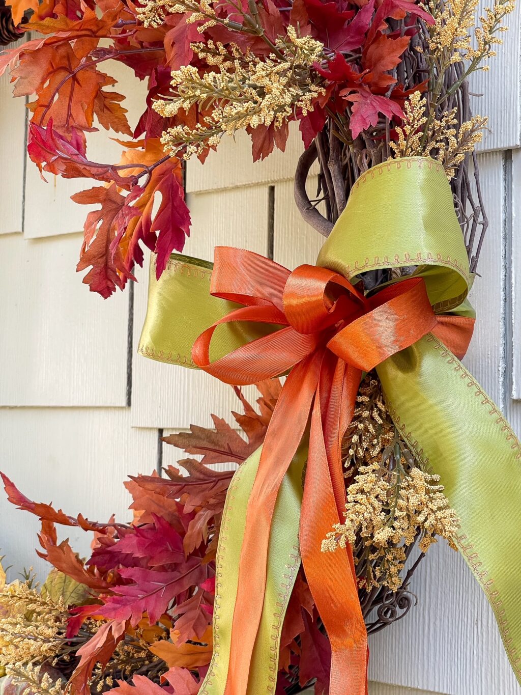 Green ribbon with smaller ribbon of orange in the middle on a grapevine wreath.