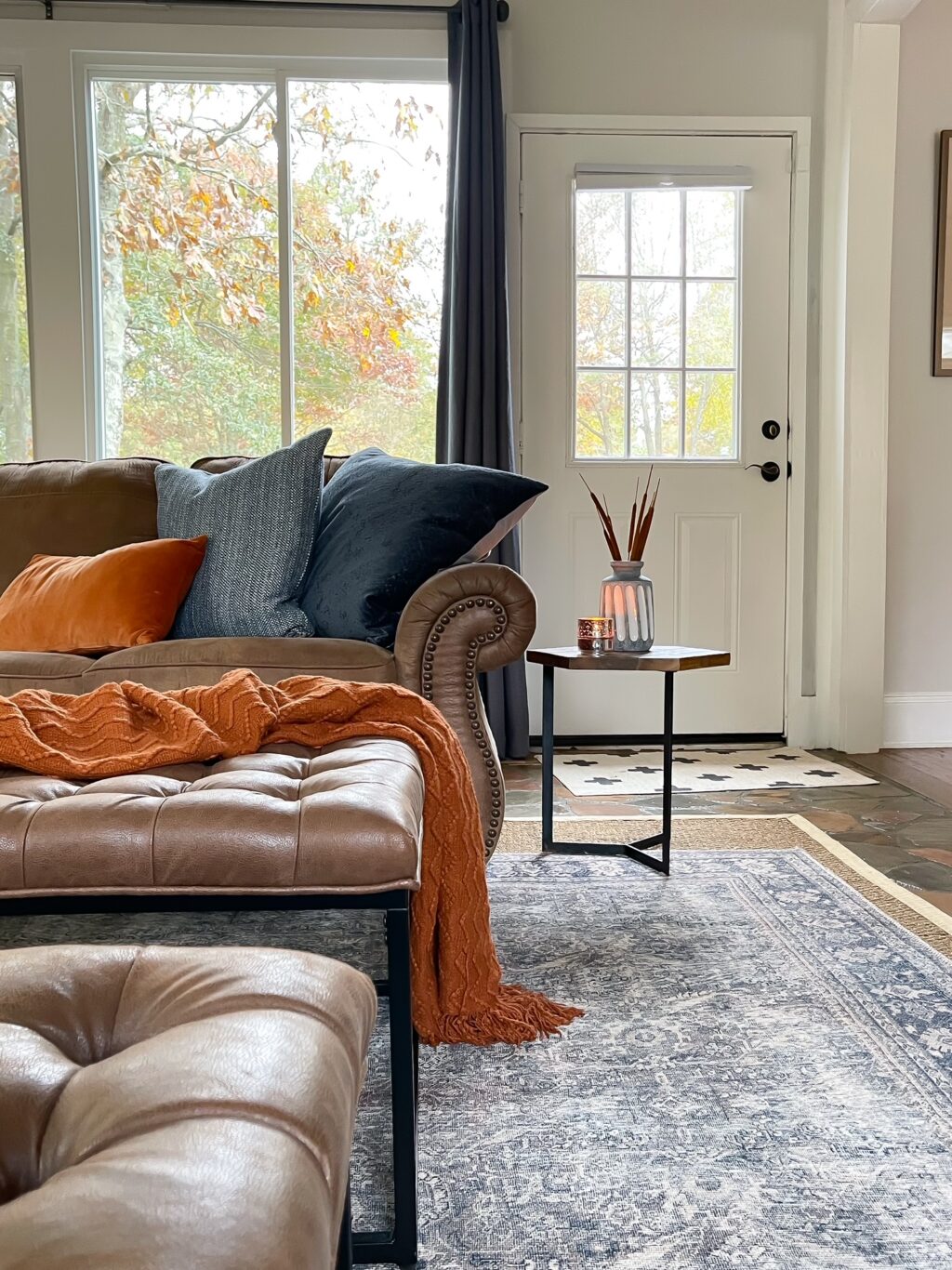 windows behind brown leather sofa with rust throw on ottoman