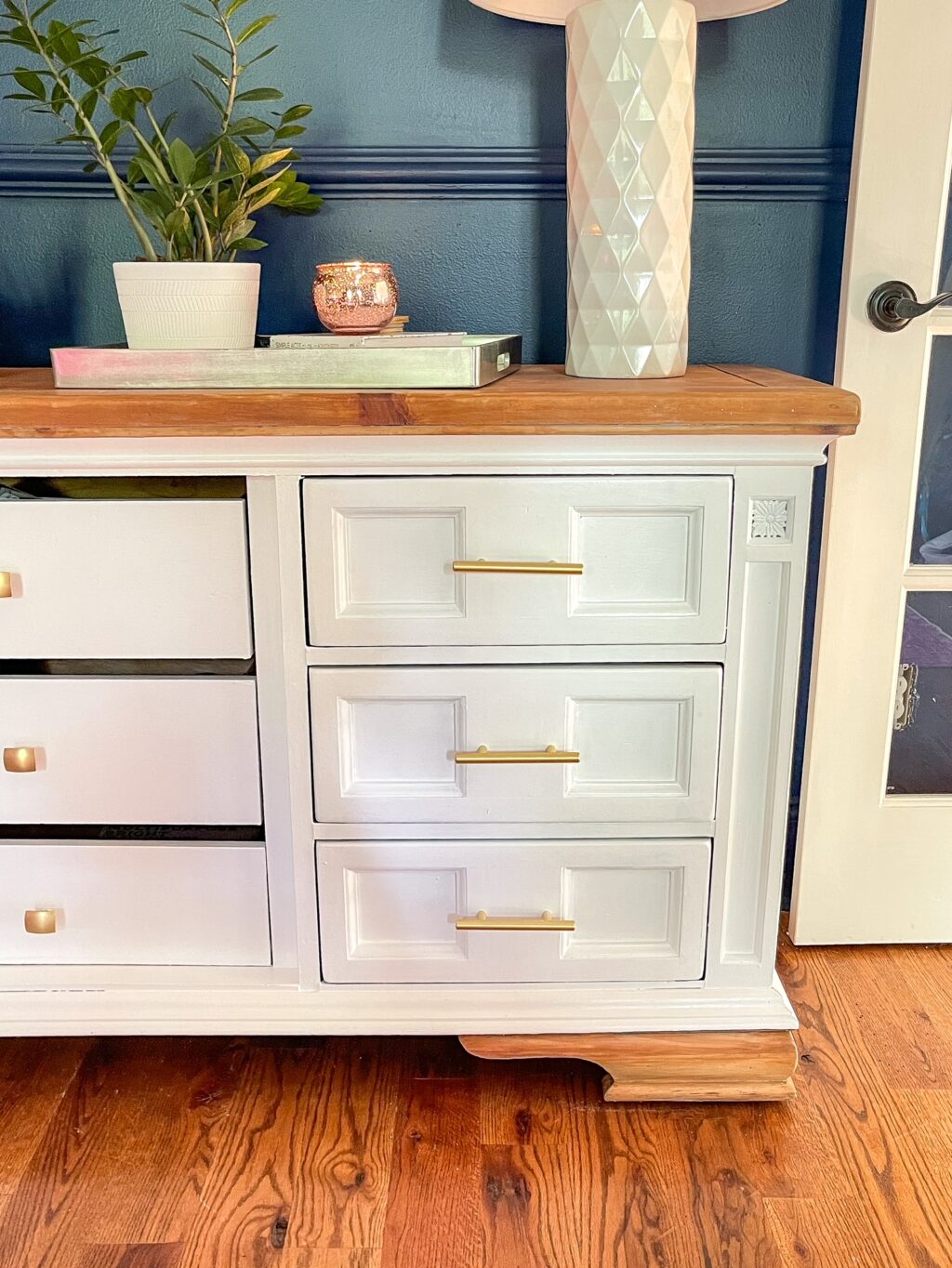 corner of white dresser, exposed legs and top with brass hardware