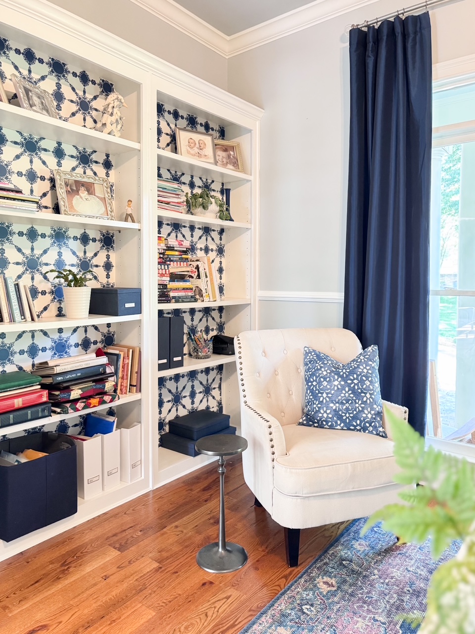 bookshelf lined with patterned wallpaper and navy curtains